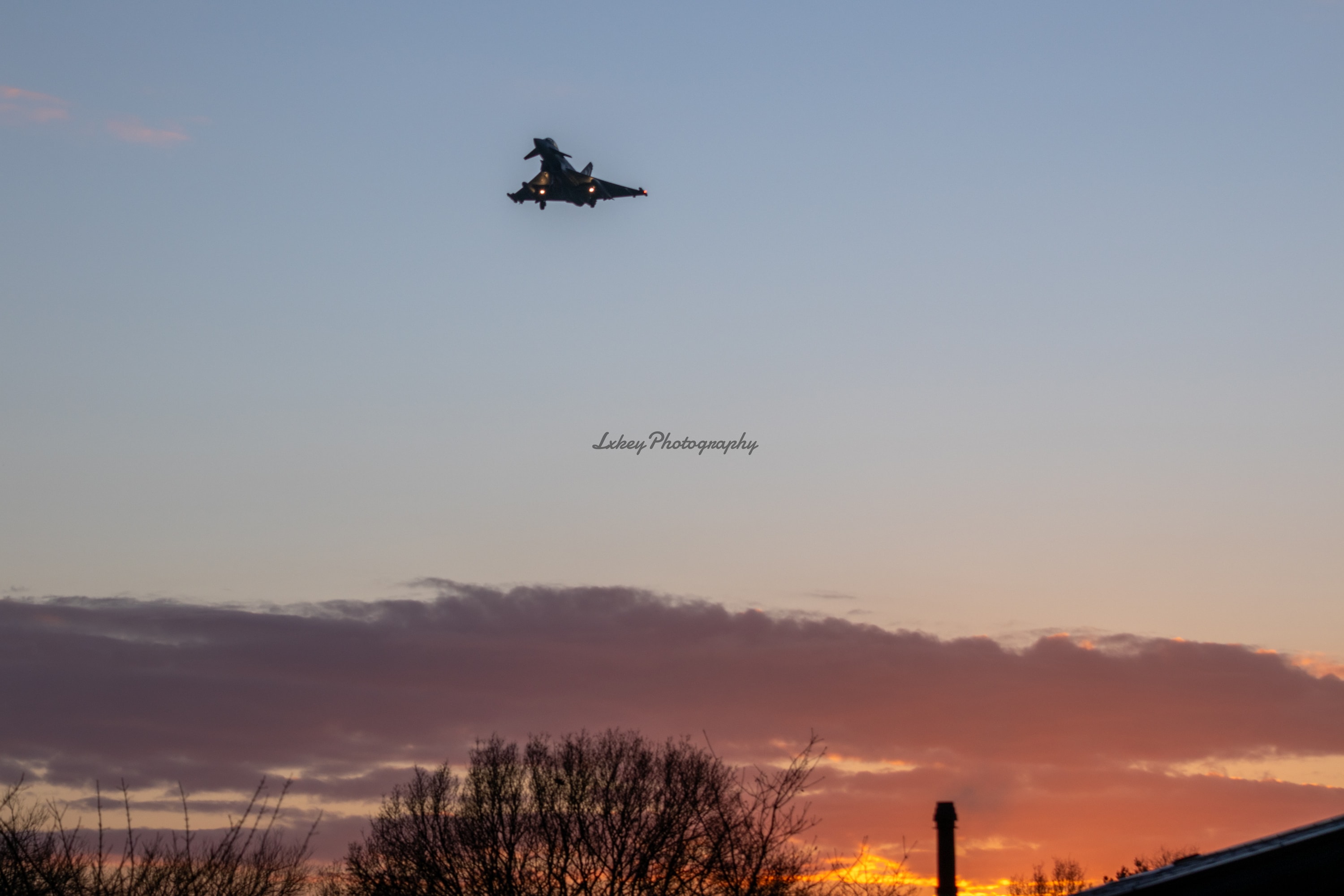 Fast jet passing over rooftops with the last of the sunset behind