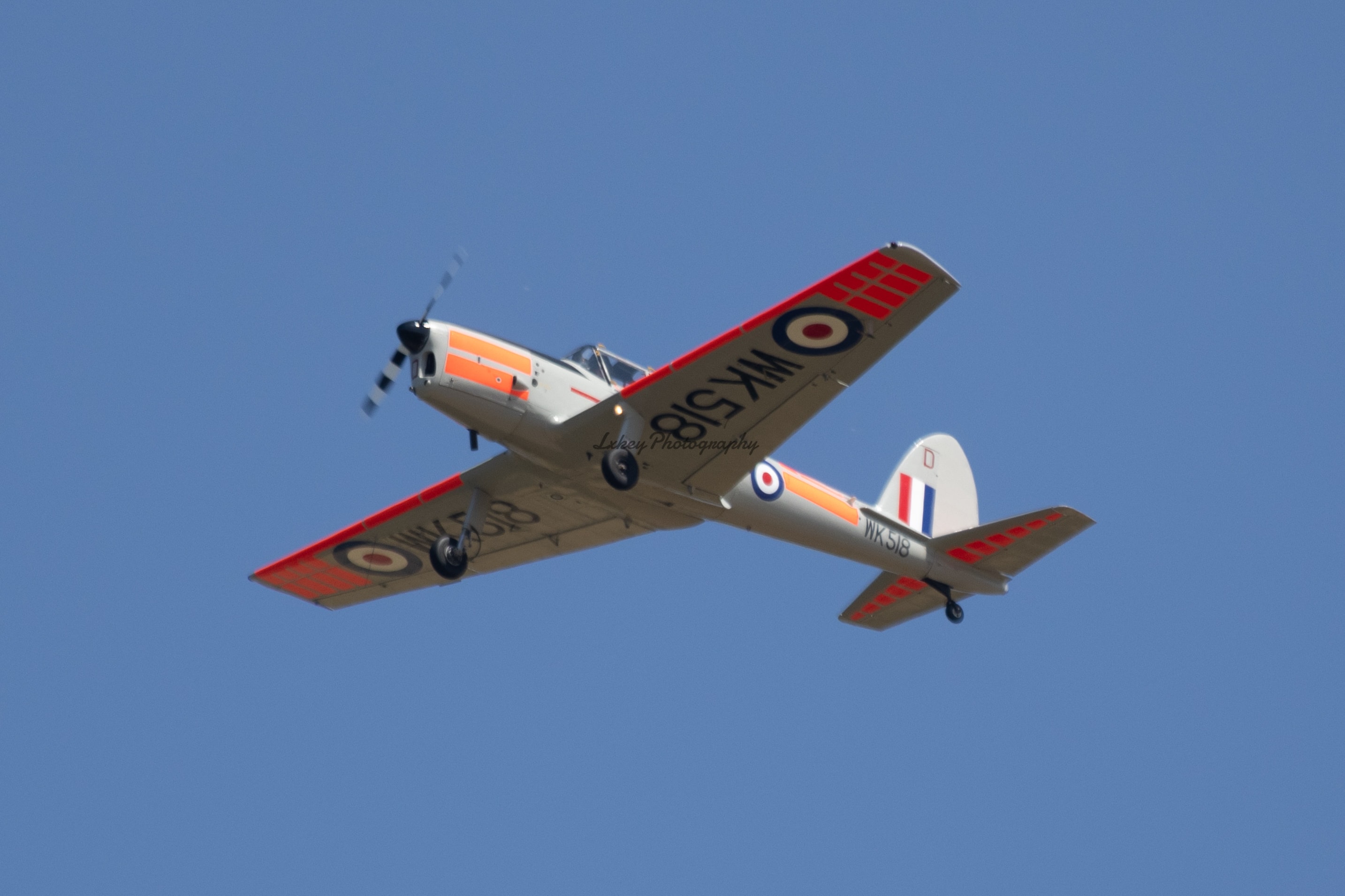 Historic red and white military trainer aircraft in flight against blue sky